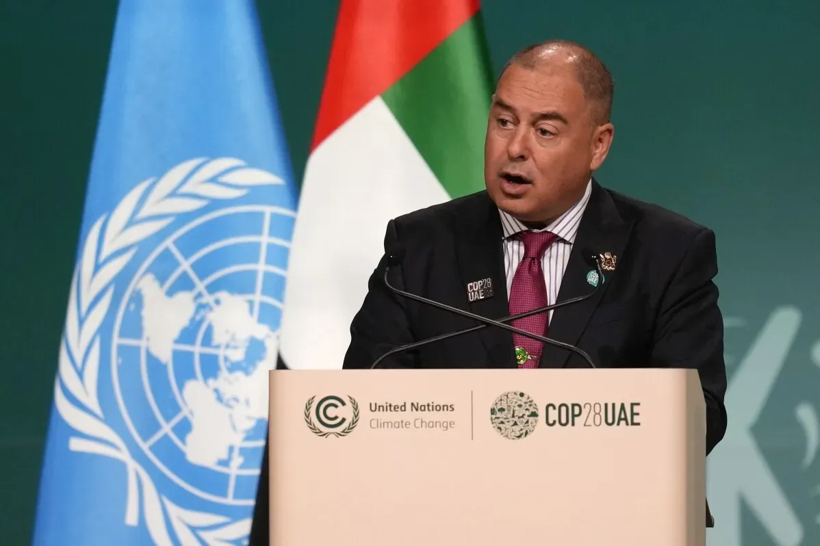 رئيس وزراء جزر كوك مارك براون يتحدث في مؤتمر تحت شعار "COP28" مع أعلام الأمم المتحدة والإمارات خلفه، في سياق تعزيز التعاون مع الصين.