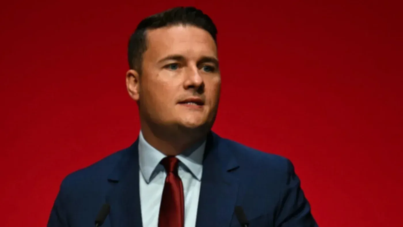 وزير الصحة ويس ستريتينغ يتحدث في مؤتمر، مع خلفية حمراء، وسط جدل حول دعم الحكومة البريطانية لإسرائيل وجرائم الحرب في غزة.