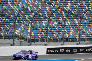 سيارة سباق تتجول على حلبة دايتونا بيتش، محاطة بمدرج ملون، مما يعكس أجواء حماس سباقات ناسكار.