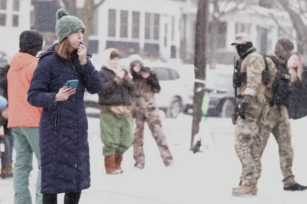 امرأة ترتدي معطفًا طويلًا وقبعة في يوم ثلجي، تتحدث عبر الهاتف بينما يشاهدها ضباط يرتدون زيًا عسكريًا في الخلفية.