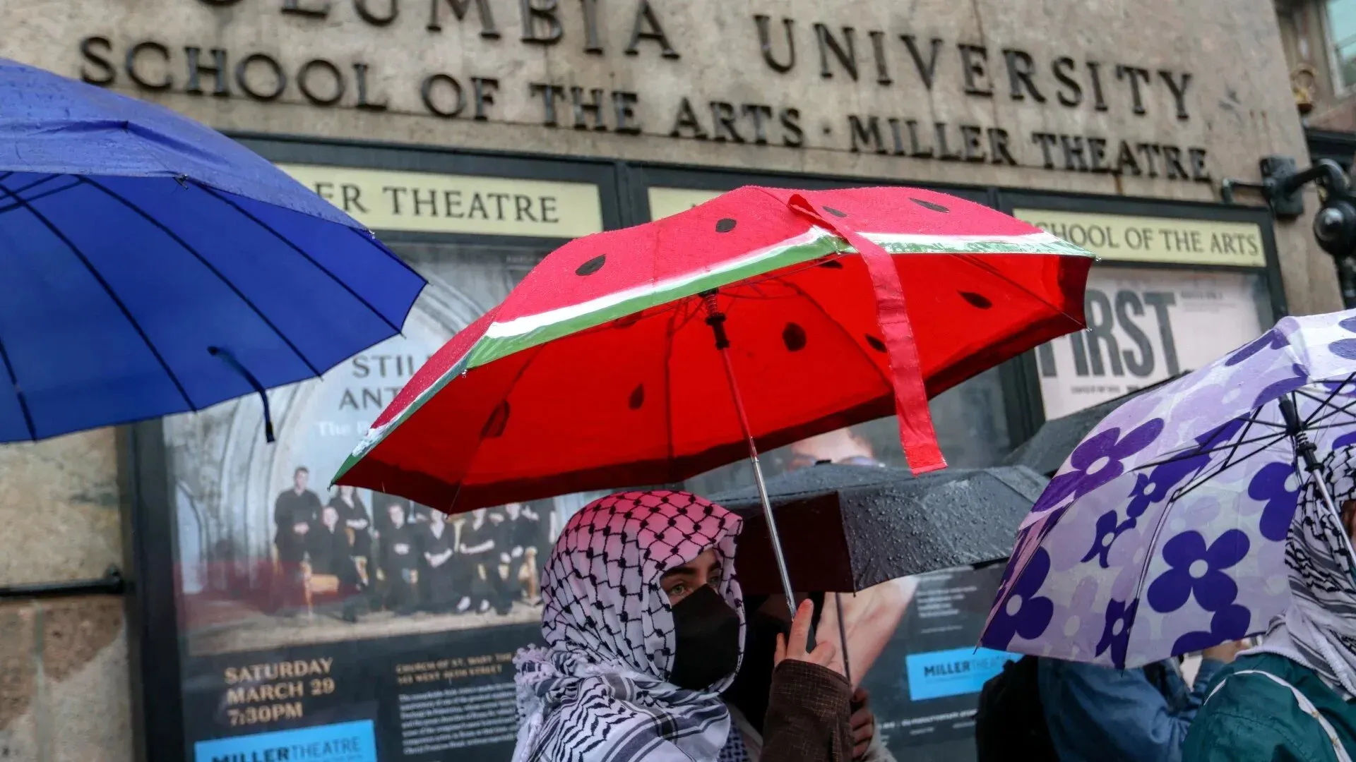 طالبة تحمل مظلة مزخرفة برمز البطيخ، ترتدي حجابًا، أمام جامعة كولومبيا، خلال احتجاجات مؤيدة لفلسطين.