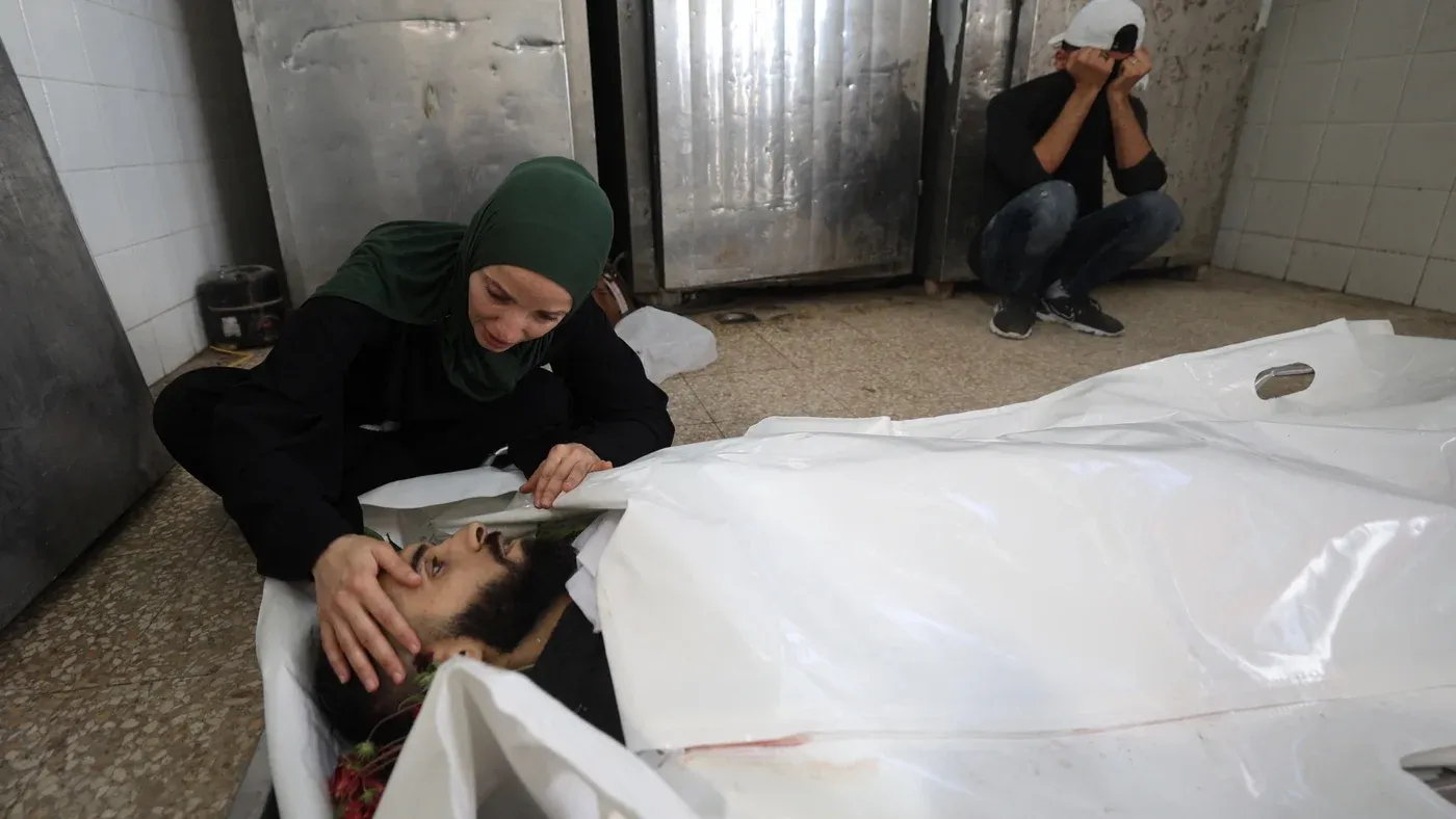 امرأة فلسطينية تودع جثمان رجل مغطى بكيس أبيض في مشهد يعكس مأساة الصحفيين الفلسطينيين الذين قُتلوا في غزة وسط جدل حول إحصائيات لجنة حماية الصحفيين.