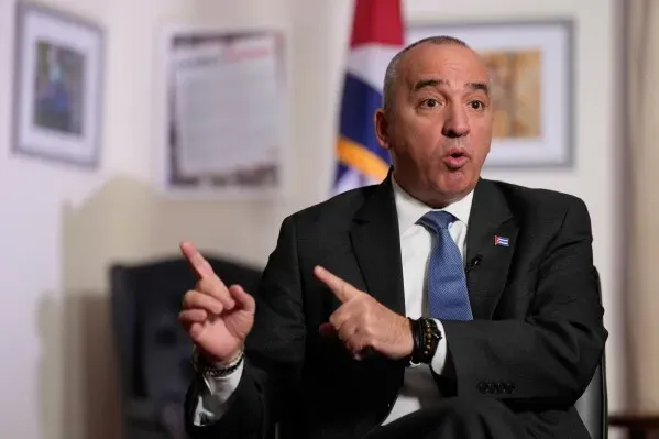 دبلوماسي كوبي يتحدث بجدية خلال مقابلة، مع العلم الكوبي خلفه، مع التركيز على التوترات بين كوبا والولايات المتحدة.