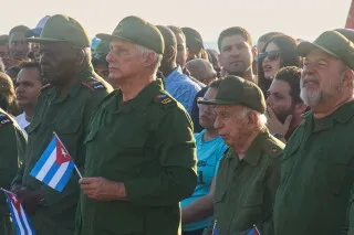 مجموعة من الرجال يرتدون زيًا عسكريًا ويحملون الأعلام الكوبية، يتواجدون في تجمع شعبي في هافانا، وسط أجواء من الحماس والتضامن.