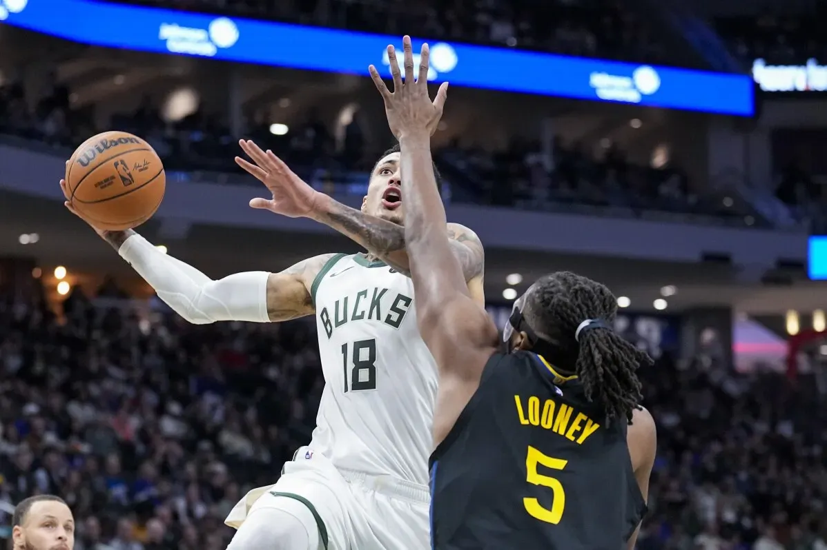 لاعب من فريق ميلووكي باكس يحاول تسجيل نقطة بينما يواجه دفاع لاعب من غولدن ستيت ووريورز في مباراة مثيرة.