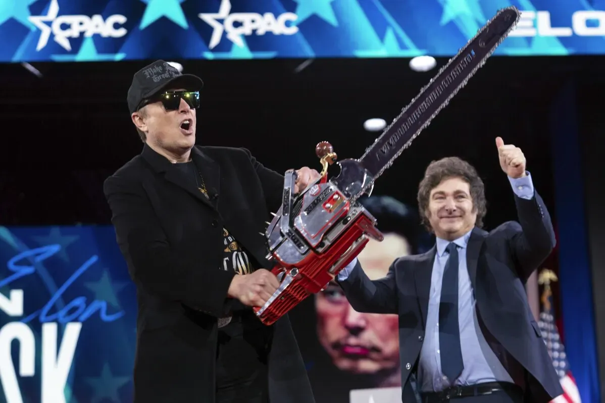 إيلون ماسك يحمل منشاراً كهربائياً خلال مؤتمر "CPAC" مع ابتسامة، مع خلفية تحمل شعار المؤتمر، مما يعكس تأثيره المتزايد في الأوساط المحافظة.
