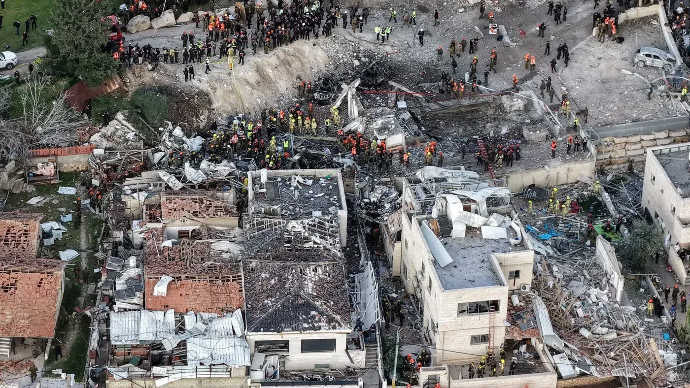 مشهد جوي لدمار كبير في منطقة سكنية بعد الهجمات، حيث يتجمع رجال الإنقاذ والشرطة بين الأنقاض، مما يعكس تأثير الصراع في المنطقة.