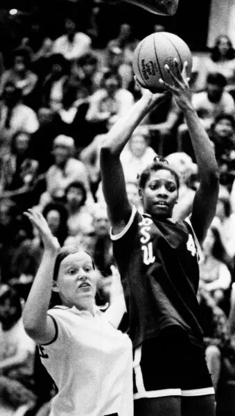 لاعبة كرة سلة من فريق ولاية دلتا تسجل نقطة خلال مباراة قديمة، مع جمهور قليل في الخلفية، تعكس بداية تاريخ كرة السلة للسيدات.