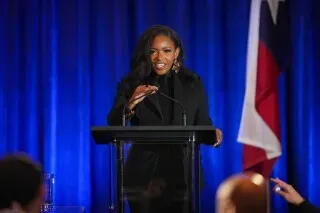 جاسمين كروكيت تتحدث في مناظرة انتخابية، مع خلفية زرقاء وعلم تكساس، حيث تناقش قضايا هامة مثل الهجرة والضرائب.