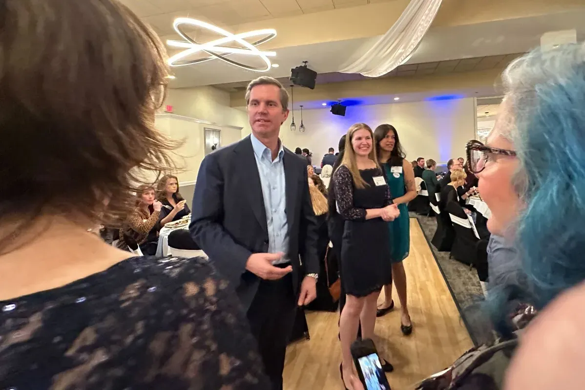 حاكم ولاية كنتاكي آندي بيشير يتحدث في حفل جمع تبرعات للحزب الديمقراطي، محاطًا بالحضور في قاعة احتفالات.