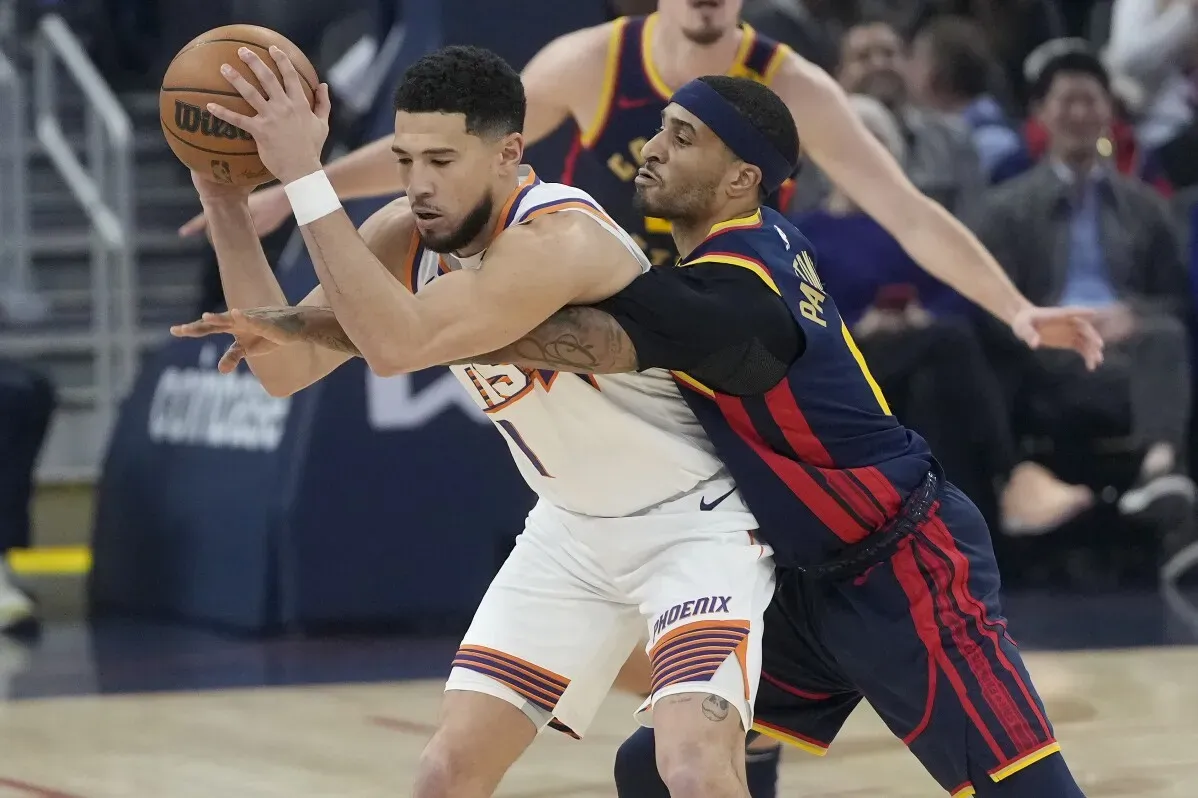 ديفين بوكر ينافس ضد لاعب غولدن ستايت، حيث يسعى للفوز بفريقه في مباراة الدوري NBA.