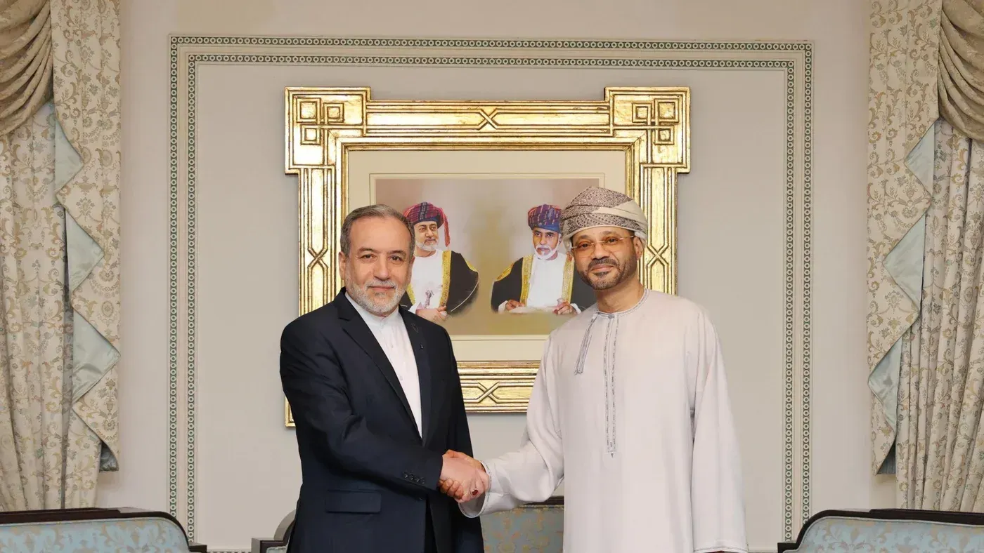 وزير الخارجية العُماني بدر بن حمد البوسعيدي يتصافح مع مسؤول إيراني، خلفهم صورة تاريخية، خلال مناقشات حول السلام في المنطقة.