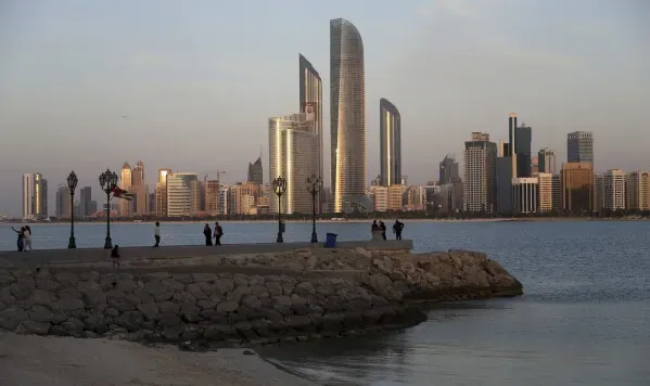 أفق مدينة أبوظبي مع ناطحات سحاب حديثة وممر مائي، حيث يظهر الناس يستمتعون بالمنظر في وقت الغروب.