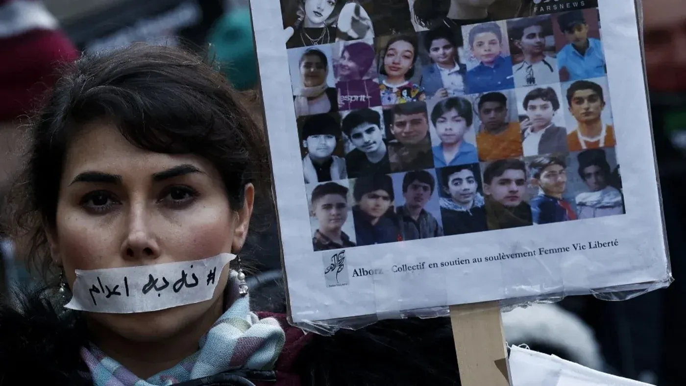 امرأة تحمل لافتة تحتوي على صور لضحايا الاحتجاجات في إيران، مع شريط على فمها مكتوب عليه "#لا_للاعدام"، تعبيرًا عن رفضها لعقوبة الإعدام.