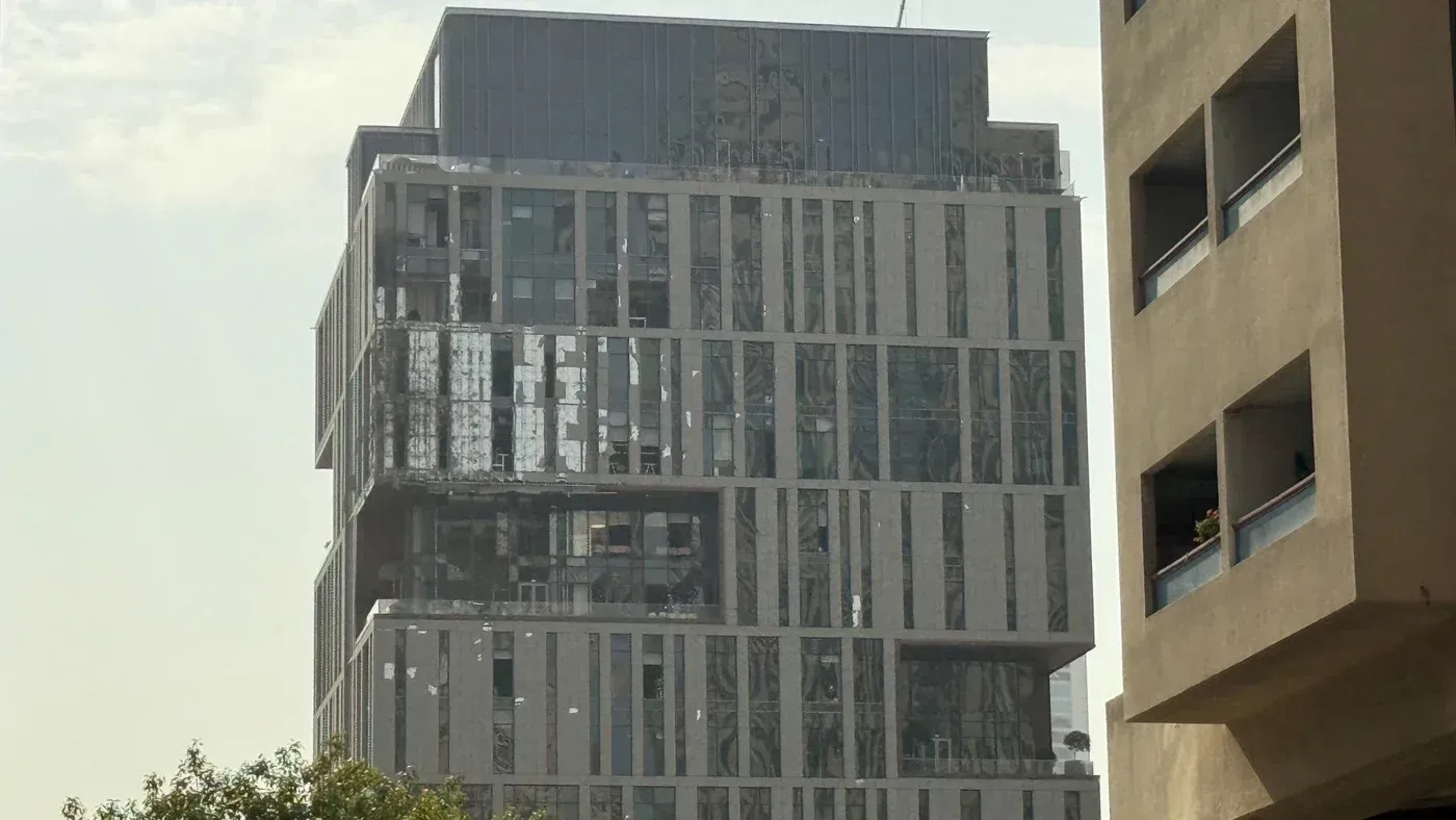 تظهر الصورة مبنى في مركز دبي المالي العالمي مع واجهة متضررة، حيث يتصاعد دخان كثيف بعد حادث ناجم عن حطام طائرة مسيرة.