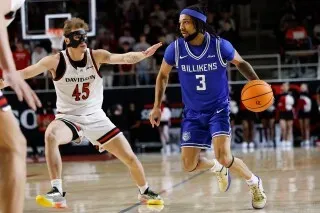 لاعب كرة سلة يرتدي زي فريق بيليكنز الأزرق يتخطى مدافعًا من فريق ديفيدسون خلال مباراة مثيرة في ملعب بيلك أرينا.