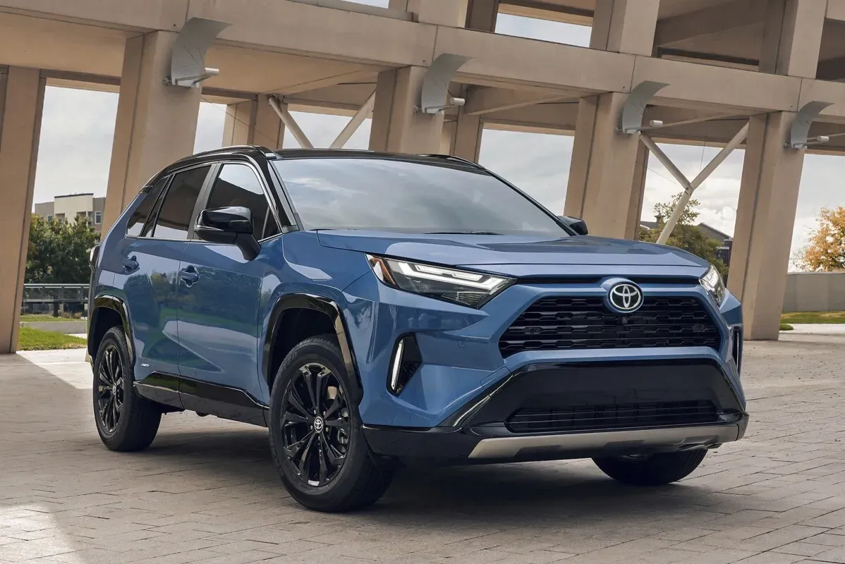 سيارة تويوتا RAV4 هايبرد الزرقاء، تظهر بتصميم عصري في موقف سيارات، مع التركيز على الشبكة الأمامية والمصابيح الأنيقة.