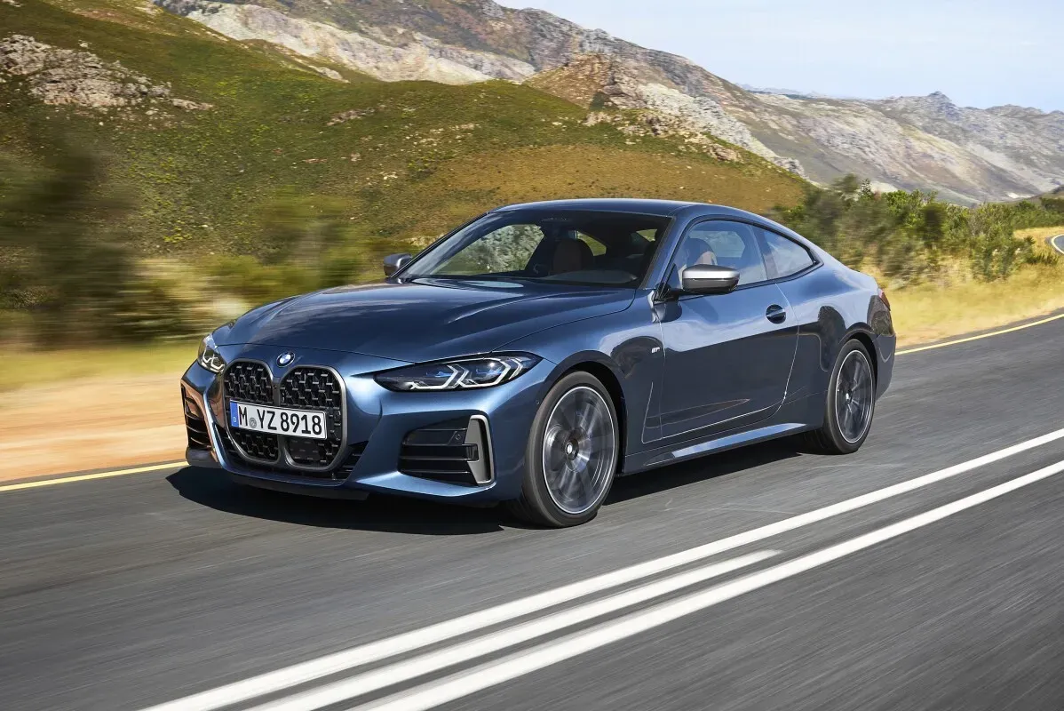 سيارة BMW الفئة 4 الكوبيه بلون أزرق، تسير على طريق جبلي، مع خلفية طبيعية خلابة، تعكس تصميمها الرياضي والأنيق.