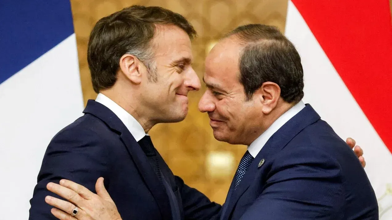 لقاء ودي بين الرئيس المصري عبد الفتاح السيسي والرئيس الفرنسي إيمانويل ماكرون، مع العلم الوطني الفرنسي والمصري في الخلفية، خلال زيارة لتعزيز التعاون.