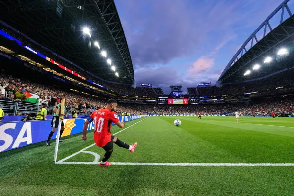 لاعب كرة قدم يرتدي القميص الأحمر رقم 10 يستعد لتنفيذ ركلة ركنية في مباراة كأس العالم، مع جمهور كبير في الخلفية.