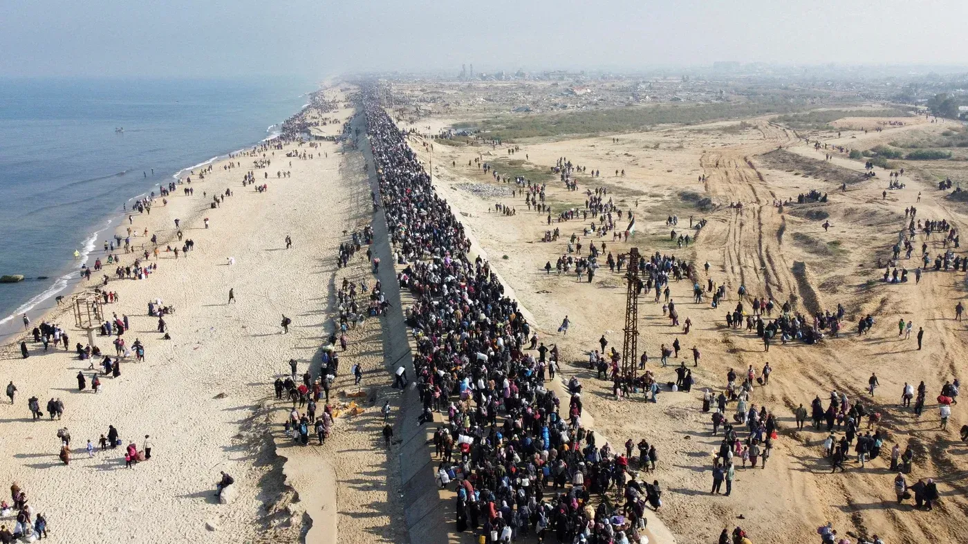 مئات الأشخاص يسيرون على شاطئ غزة، حيث يظهر المشهد كثافة الحشود في رد فعل على التهديدات الأمريكية بتهجير الفلسطينيين.