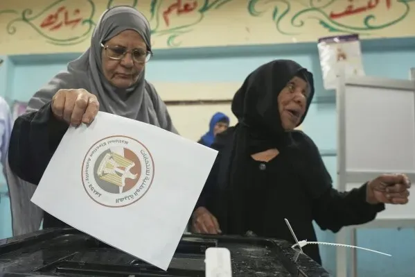 امرأتان مسنّتان ترتديان الحجاب، واحدة منهما تلقي ورقة الاقتراع في صندوق الانتخاب، في مركز اقتراع بالقاهرة.