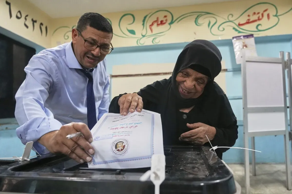 مواطن مصري يساعد سيدة مسنّة على التصويت في مركز اقتراع، تعبيرات الفرح والاهتمام تعكس أهمية الانتخابات لمستقبل البلاد.