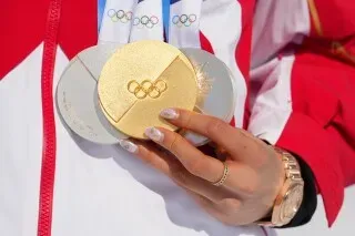 ميدالية ذهبية وفضيتان تُظهرها يد متزلجة، تعكس إنجازات إيلين غو في الألعاب الأولمبية الشتوية.