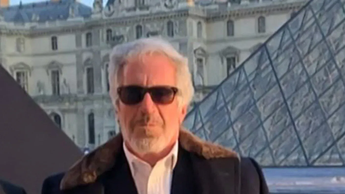 جيفري إبشتاين يرتدي نظارات شمسية في موقع خارجي، مع معالم معمارية بارزة في الخلفية، تعكس السياق الدبلوماسي المعقد في الخليج.