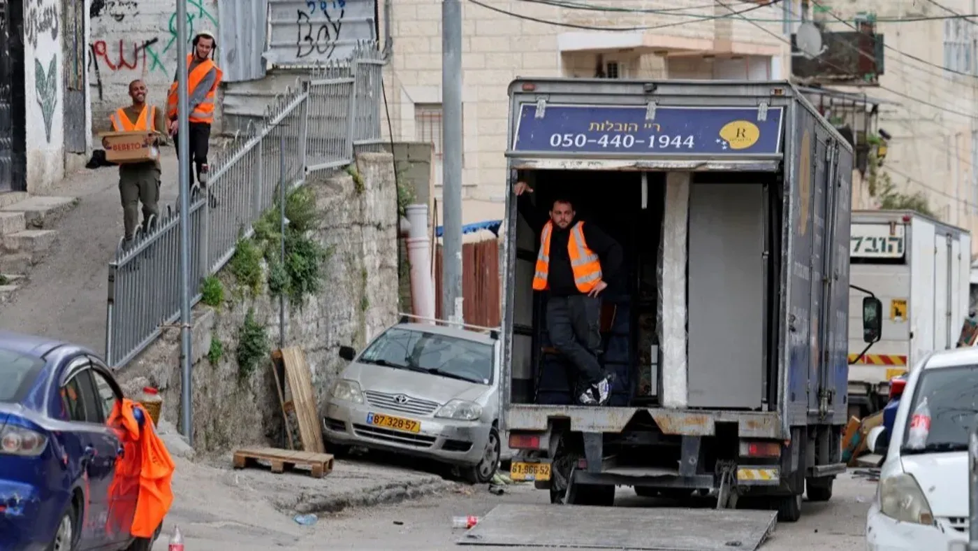 عمال يرتدون سترات برتقالية ينقلون صناديق من شاحنة في حي سلوان، وسط توتر بعد طرد عائلات فلسطينية من منازلها.