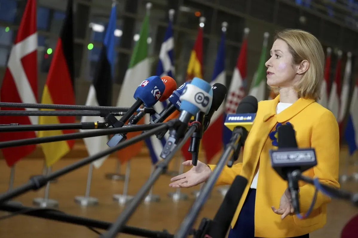 ممثلة عن الاتحاد الأوروبي تتحدث أمام ميكروفونات متعددة في مؤتمر صحفي، مع أعلام الدول الأوروبية خلفها، في إطار مناقشات حول تخفيف العقوبات على سوريا.