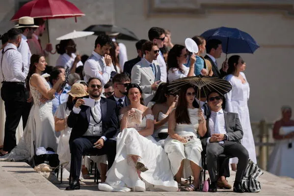 حفل زفاف في يوم حار، حيث يجلس الضيوف تحت أشعة الشمس، بعضهم يحمل مظلات لحماية أنفسهم من الحرارة.