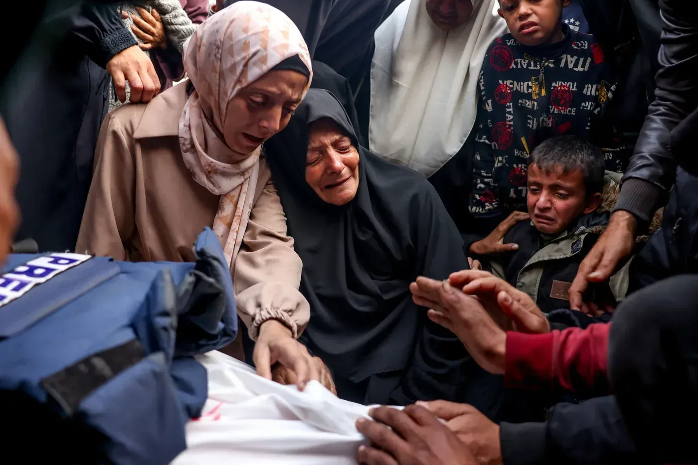 نساء وأطفال فلسطينيون يبكون حول جثة في غزة، معبرين عن الحزن والفزع بسبب الغارات الإسرائيلية المتواصلة.