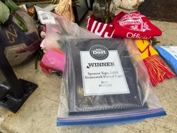 جائزة "أفضل طبيب أسنان" للدكتور سبنسر تيبي موضوعة في كيس بلاستيكي، محاطة بالزهور والذكريات، تكريمًا لذكراه بعد الحادث المأساوي.