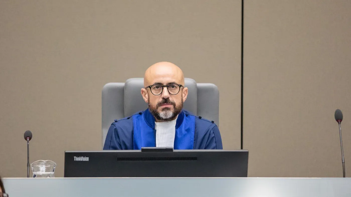 قاضٍ دولي يرتدي رداءً قضائياً أزرق يجلس خلف منصة المحكمة الجنائية الدولية في لاهاي خلال جلسة تحقيق في جرائم طالبان المتعلقة بالاضطهاد القائم على النوع الاجتماعي.