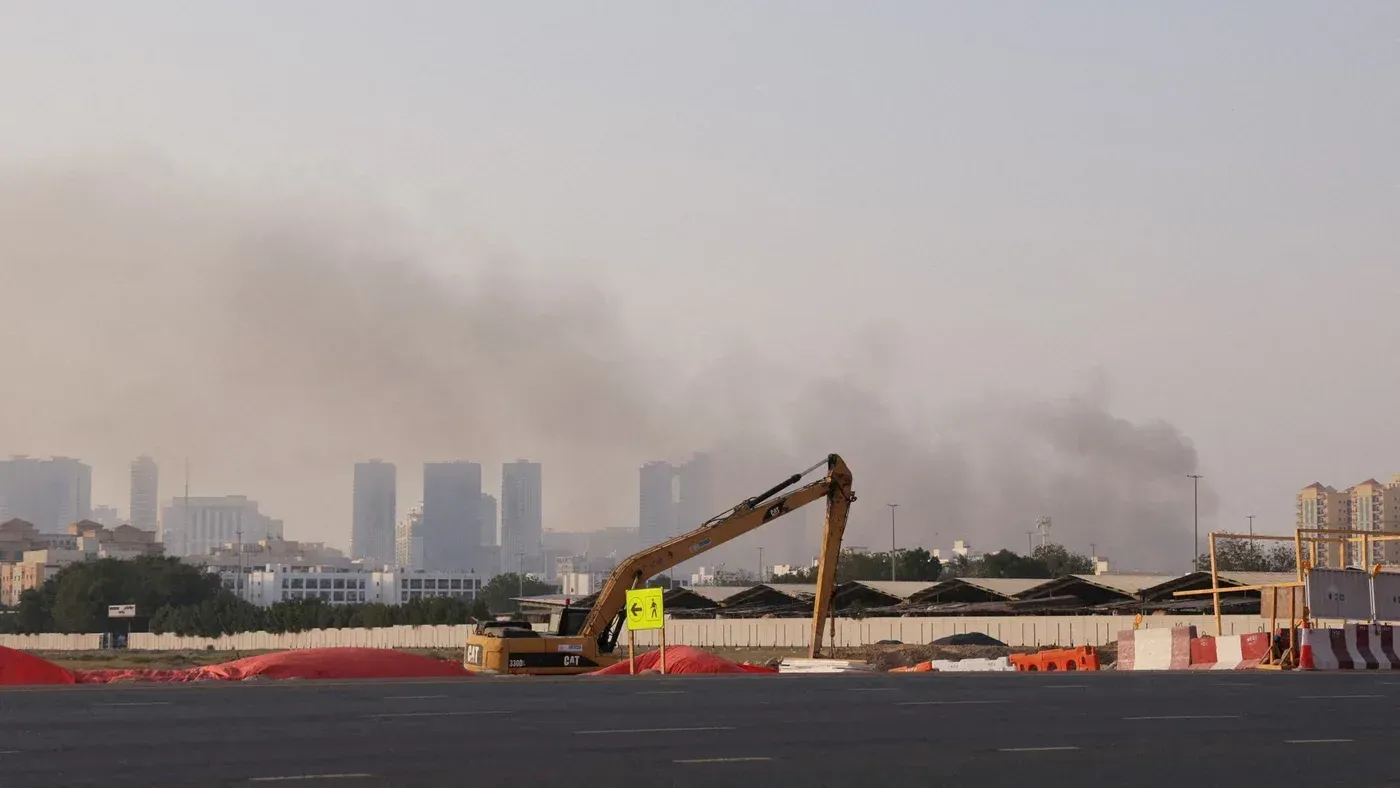 سحابة من الدخان تتصاعد فوق المدينة، مع وجود جرافة في المقدمة، تشير إلى تأثير الهجمات على البنية التحتية في الخليج.