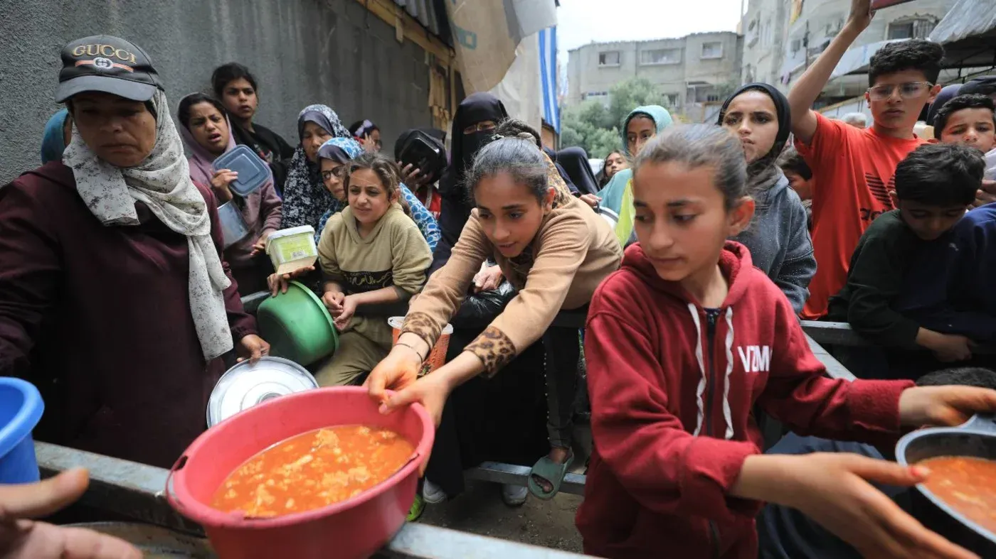 نساء وأطفال فلسطينيون يتجمعون في صف للحصول على الطعام في غزة، وسط أزمة إنسانية متفاقمة نتيجة النزاع المستمر.