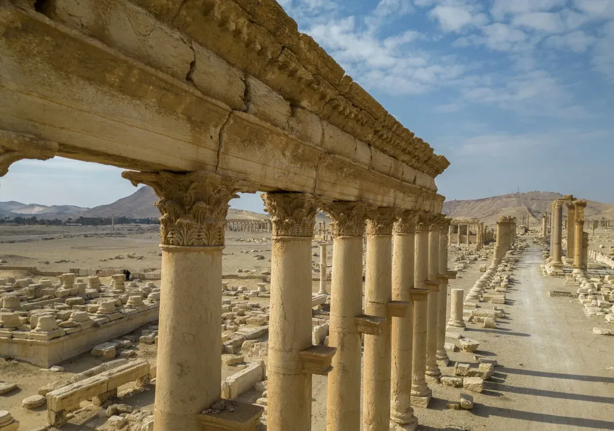 آثار مدينة تدمر القديمة، مع أعمدة رومانية مدمرة، تعكس تاريخاً غنياً وتعرض تأثير الحرب على المواقع التراثية في سوريا.