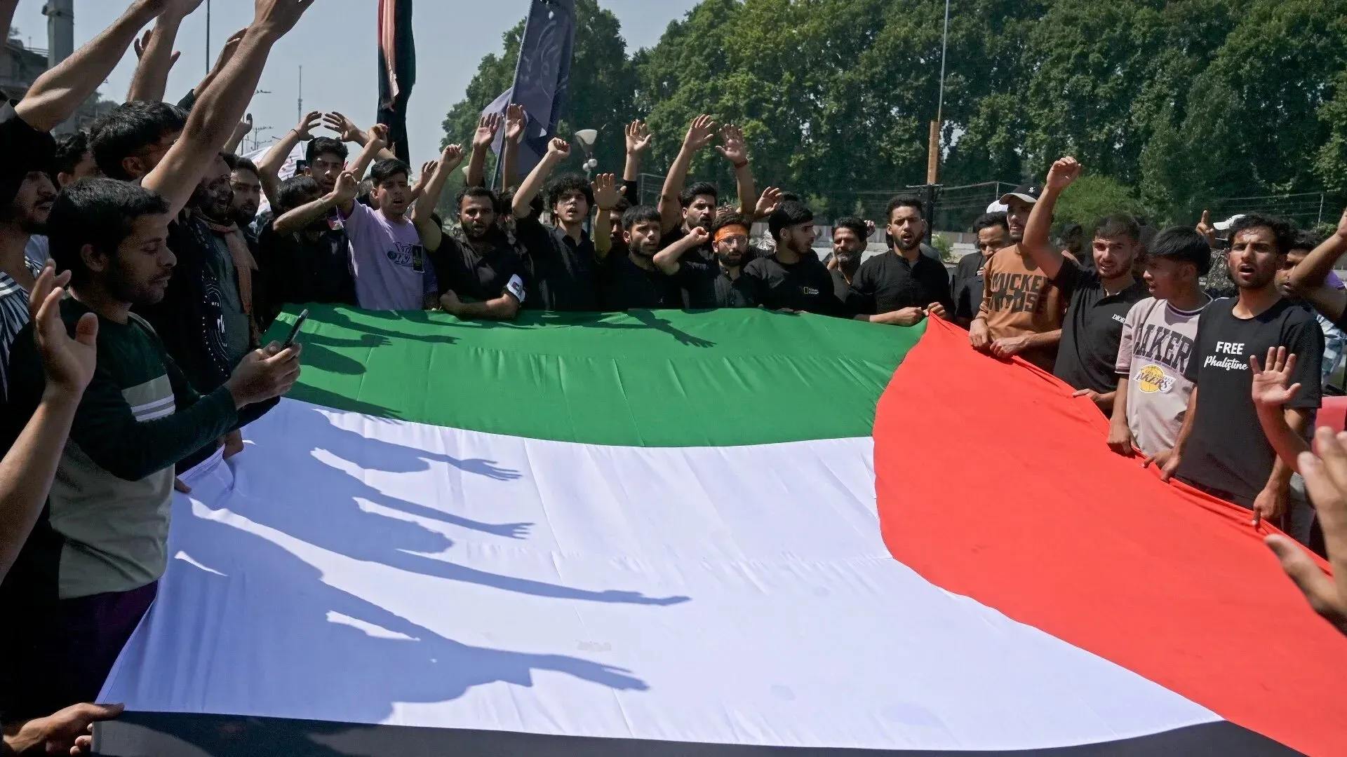 محتجون يحملون علم فلسطين الكبير في مسيرة، مع تفاعل جماهيري قوي، تعبيرًا عن التضامن مع القضية الفلسطينية.