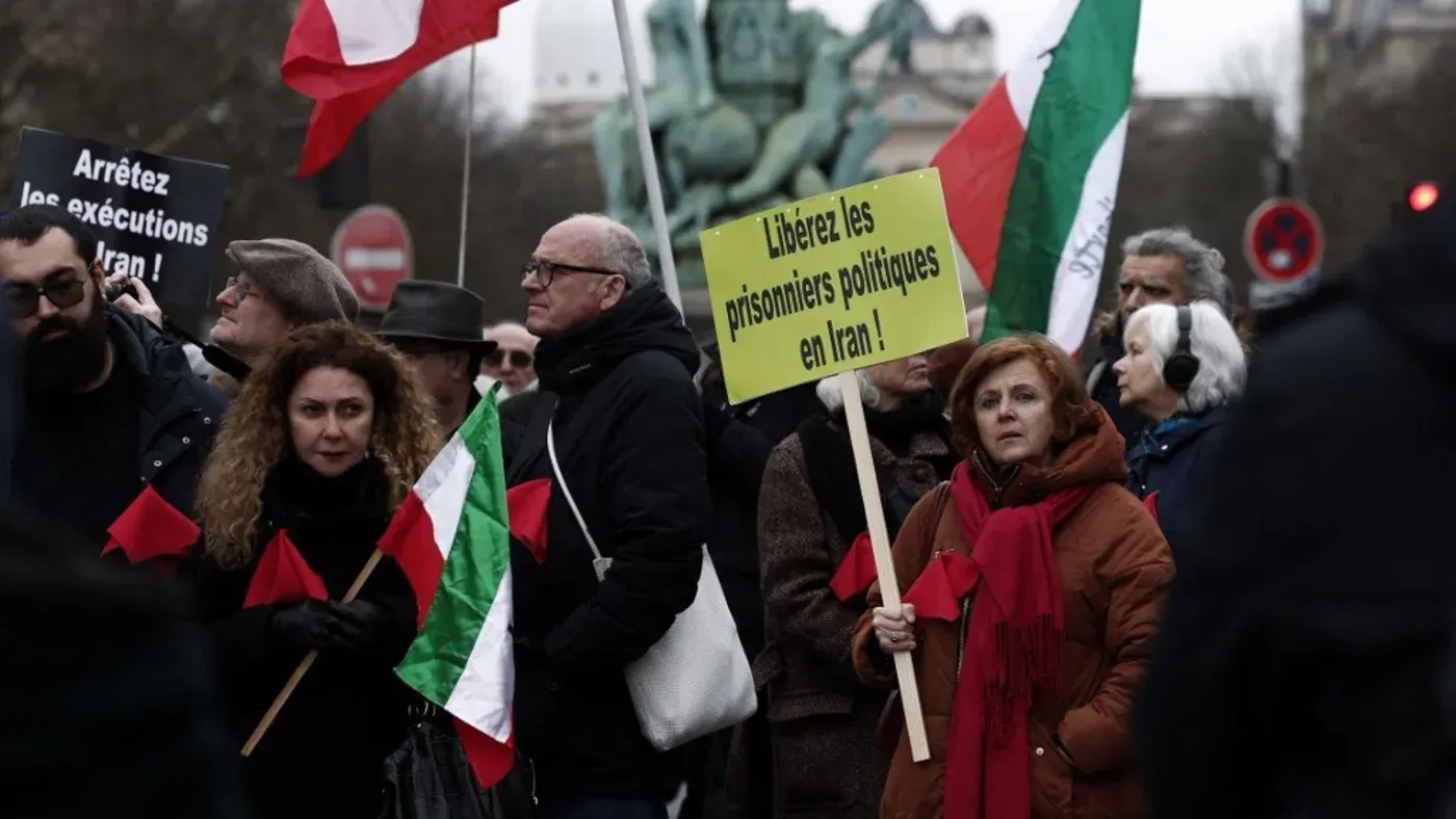 محتجون يحملون لافتات تطالب بالإفراج عن السجناء السياسيين في إيران، مع أعلام تمثل الهوية الإيرانية، في تظاهرة في مدينة أوروبية.