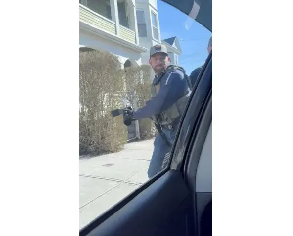 عميل من وكالة إنفاذ قوانين الهجرة والجمارك يحمل سلاحًا أثناء اقتحام سيارة في نيو بيدفورد، ماساتشوستس، مما يثير القلق حول تكتيكات الاعتقال.