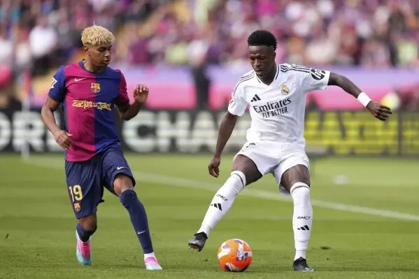 فينيسيوس جونيور لاعب ريال مدريد يراوغ لاعب برشلونة في مباراة كرة قدم، مع التركيز على أهمية مكافحة العنصرية في الرياضة.