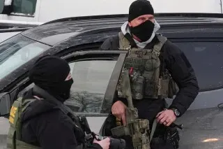 عناصر من إنفاذ القانون يرتدون زيًا عسكريًا ويقفون بالقرب من سيارة، في سياق الاحتجاجات على حملة الهجرة في مينيابوليس.