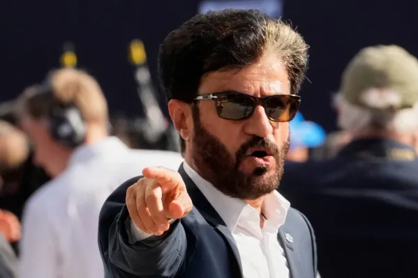 محمد بن سليم رئيس الاتحاد الدولي للسيارات يرتدي نظارات شمسية ويتحدث بحزم وسط أجواء سباقات الفورمولا 1.