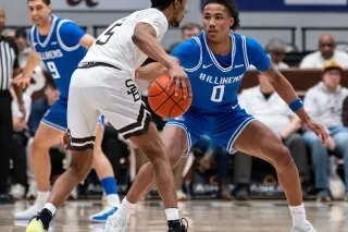 مباراة كرة سلة بين لاعبين من فريق سانت لويس، يرتدي أحدهم زيًا أزرق بينما الآخر يرتدي زيًا أبيض، وسط جمهور متحمس.