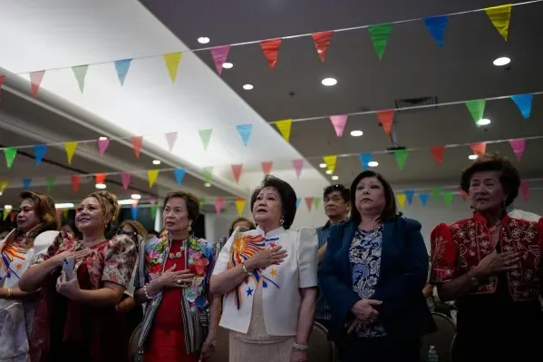 نساء فلبينيات يرتدين ملابس تقليدية، يقفن معًا خلال احتفال ثقافي، محاطات بأعلام ملونة، تعبيرًا عن الفخر الثقافي في لاس فيغاس.