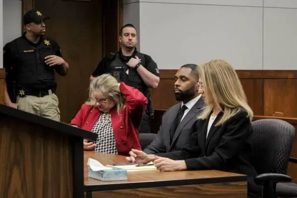 مور وزوجته في قاعة المحكمة، حيث تم حل قضيته الجنائية. المحاميات بجانبهما، مع وجود ضابط أمن في الخلفية.