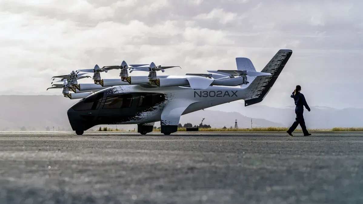 طائرة eVTOL كهربائية جديدة على مدرج، مع شخص يسير بجانبها، تمثل مستقبل النقل الجوي كسيارة أجرة في السماء.
