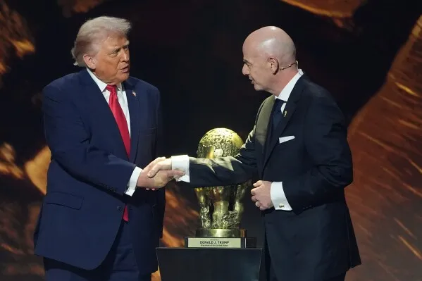 ترامب يصافح رئيس الفيفا، مع وجود كأس العالم في الخلفية، خلال إعلان عن تخفيف شروط تأشيرات مشجعي كأس العالم.