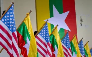 تظهر الصورة أعلام الولايات المتحدة وميانمار مرتبة بشكل متناسق، مع خلفية تتضمن علم ميانمار، مما يعكس التوترات السياسية بين البلدين.